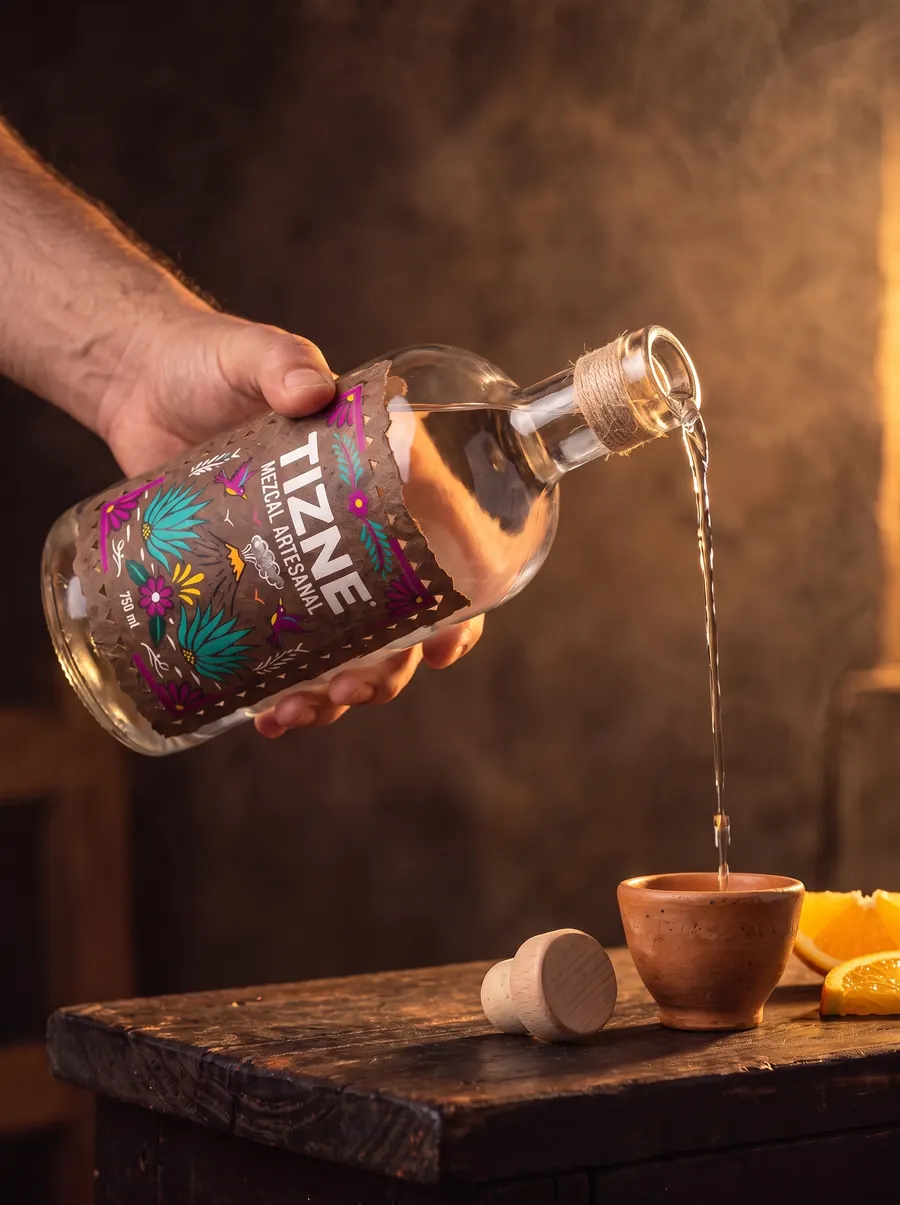 A hand pouring TIZNE mezcal into a clay cup
